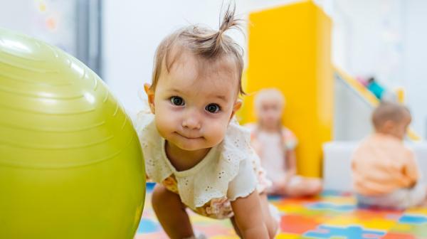 n bébé regarde la caméra, une main sur un ballon géant